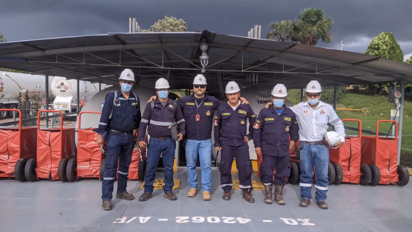Seis integrantes del equipo con cascos posando bajo el techo del embarcadero junto a los tanques